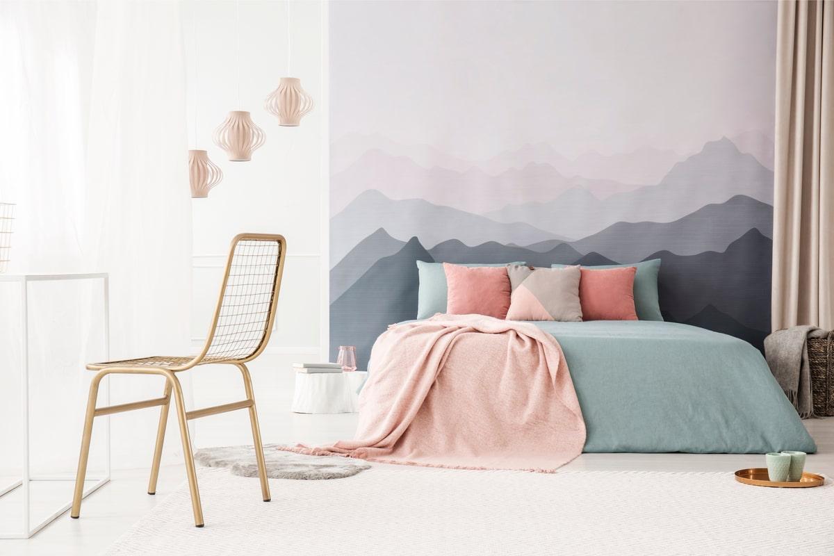 A pastel bedroom design decorated with gold furnishings and wallpaper featuring a mountain landscape, such as Sanberg wallpapers.
